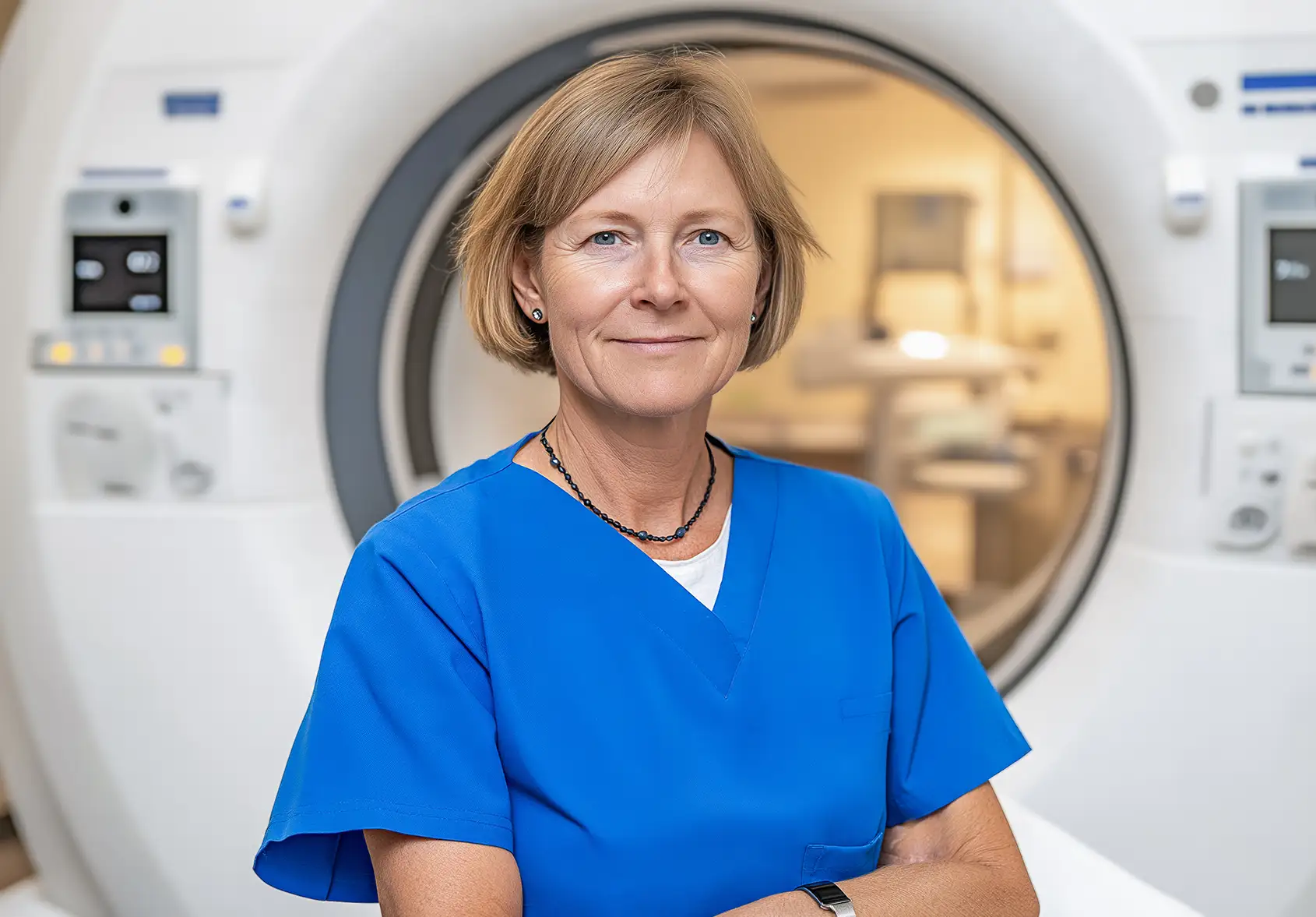 AdobeStock_1159641605 copy Confident middle-aged female radiologist standing in front of an MRI scanner, wearing blue scrubs in diagnostic center.